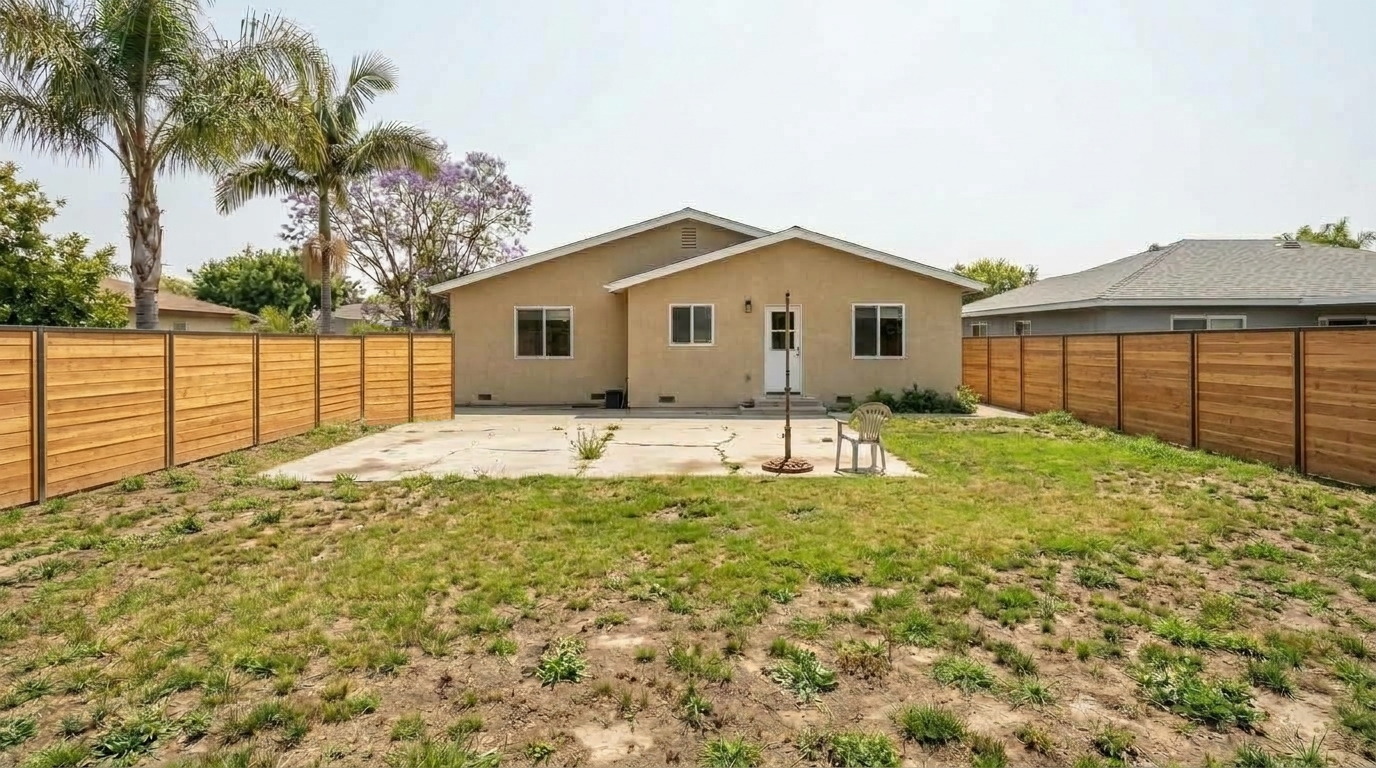 A Los Angeles Metro Area backyard before the remodel, with patchy dry grass, a cracked concrete patio, and a plain wood fence