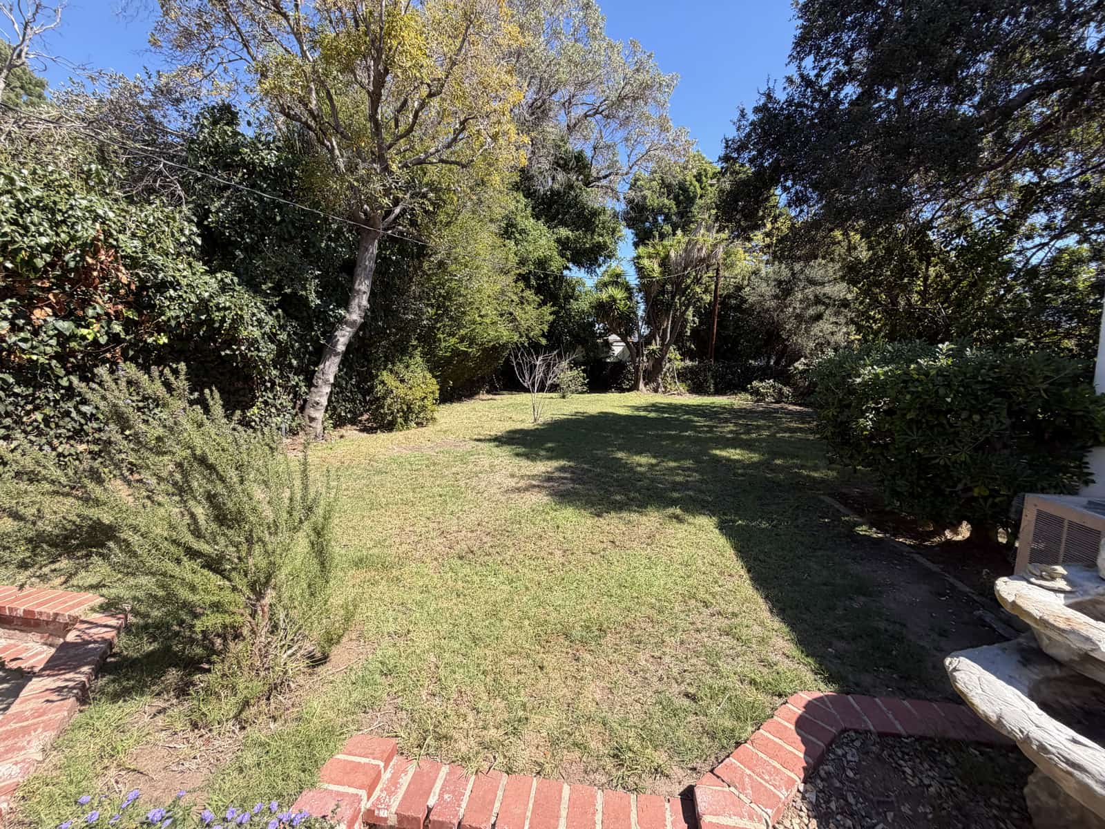 A flat lawn with mature trees and a brick border