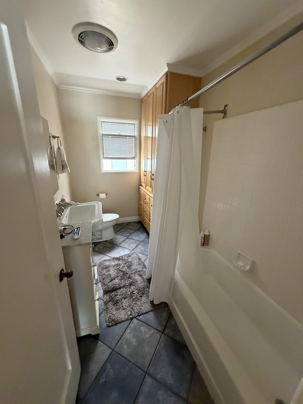A bathroom seen from the doorway with a tub, a shower curtain, dark floor tile and oak cabinets